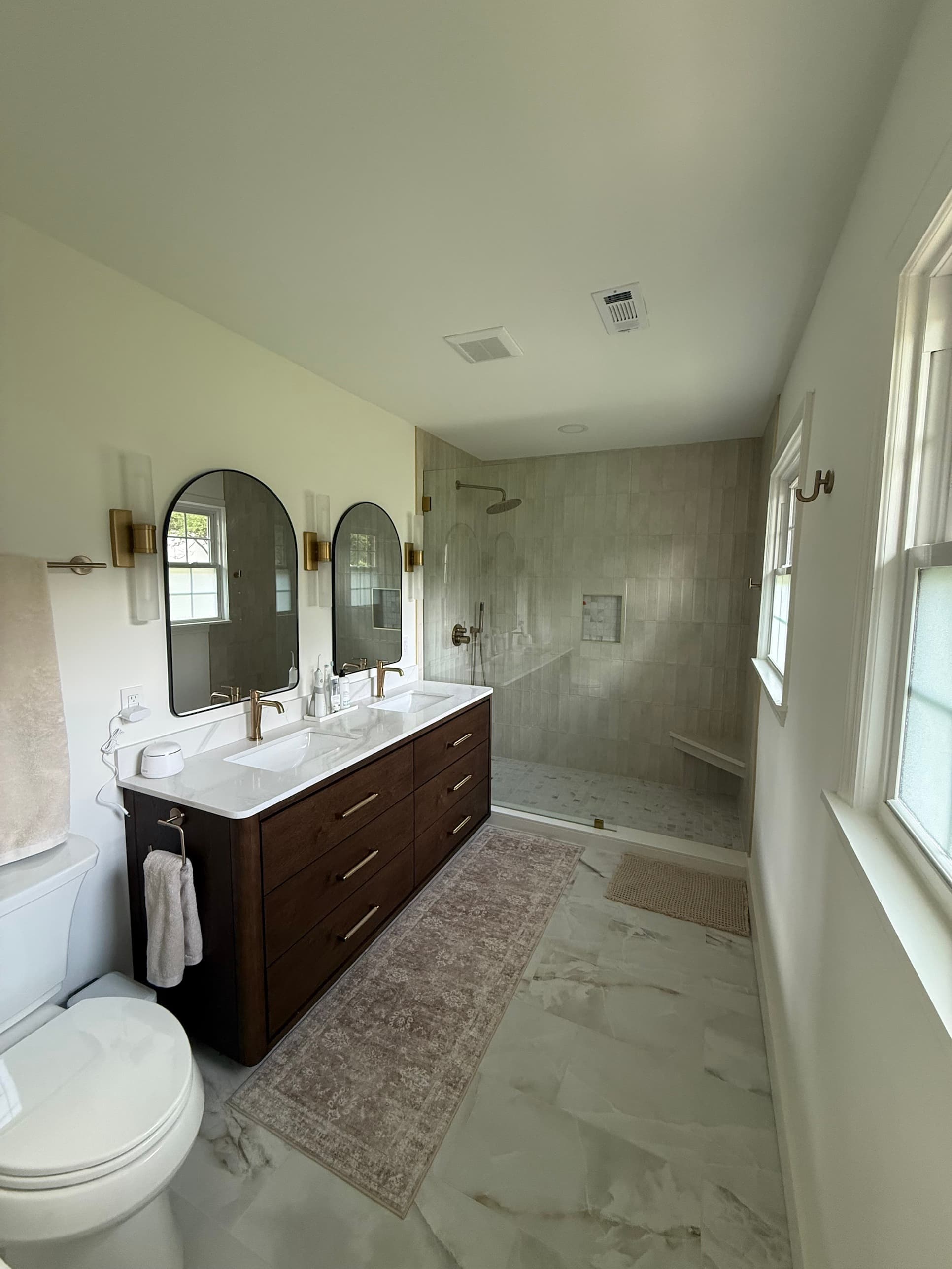 Primary bathroom renovation with frameless walk-in shower, marble floors, double vanity, and gold fixtures in Charlotte, NC by Remodel CLT