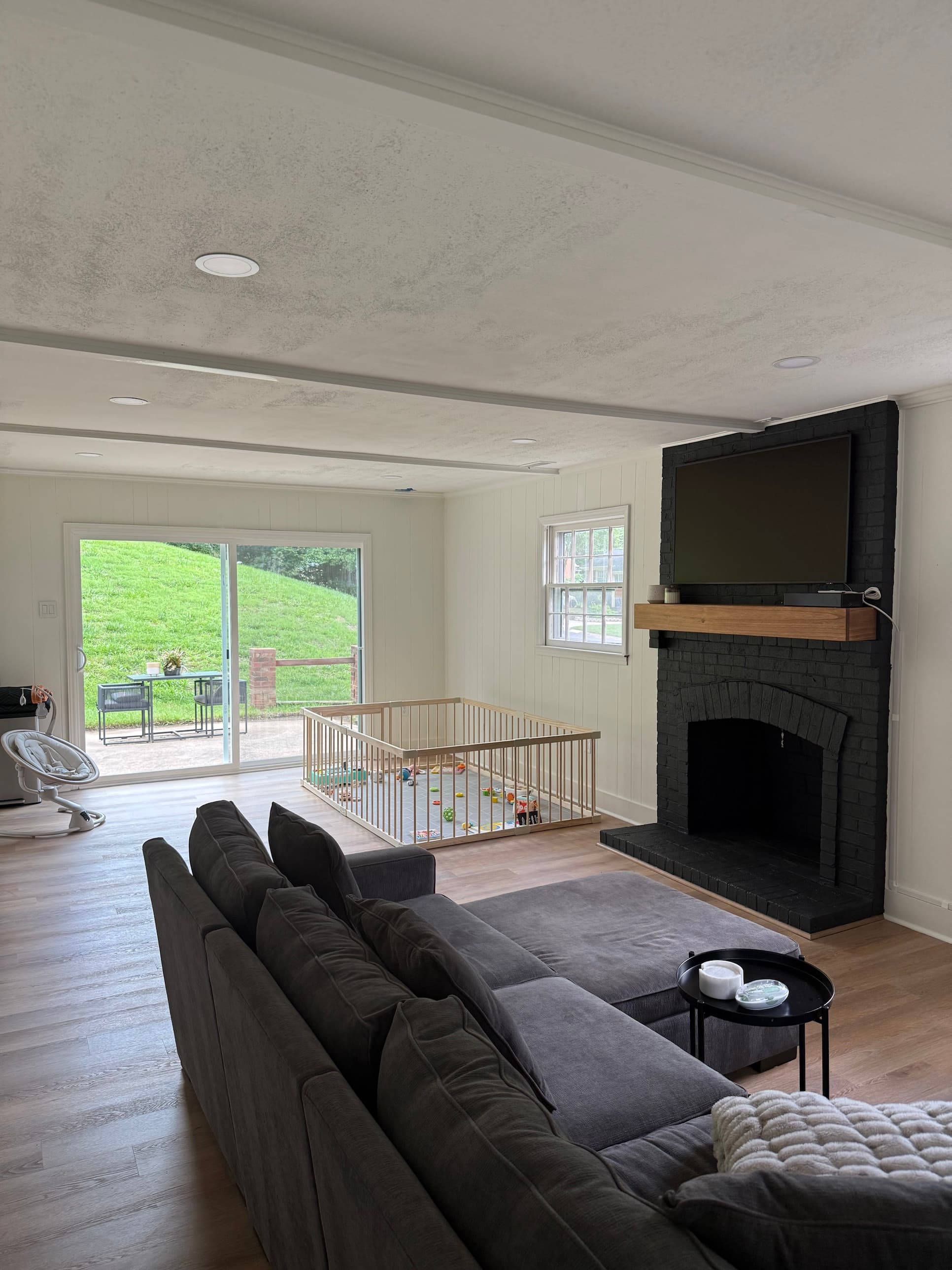 Living room renovation with shiplap accent walls, black painted brick fireplace, wood mantel, and LVP flooring in Charlotte, NC by Remodel CLT