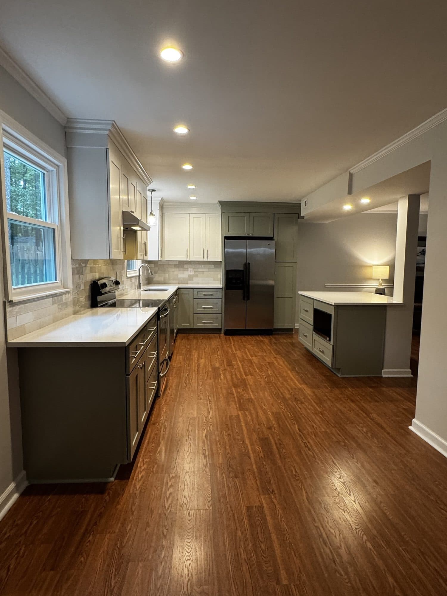 Open-concept kitchen remodel in Stonehaven, Charlotte NC: sage green lower cabinets, white upper cabinets, white quartz countertops and new wood-look floors by Remodel CLT